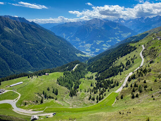 Panoramic view into Passeier Valley (germ. Passeiertal) from Jaufenpass in South Tyrol, Italy with winding mountain road, green pastures and forested slopes under a blue sky © A. Emson