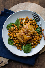 Pan-seared cod served with chickpeas and fresh spinach on a white plate