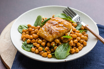Pan-seared cod served with chickpeas and fresh spinach on a white plate