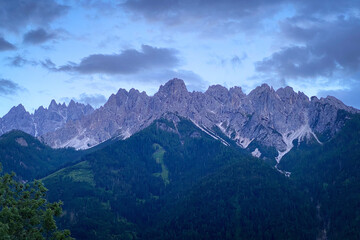 Obraz premium Scenic evening view of Neunerkofel mountain south of Toblach (Dobbiaco), Italy; jagged Dolomite peaks above dark forested slopes under a moody sky