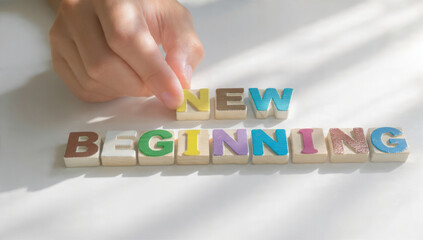 A hand arranges colorful wooden blocks to spell "NEW BEGINNING" on a white surface, symbolizing fresh starts, hope, and future opportunities.
