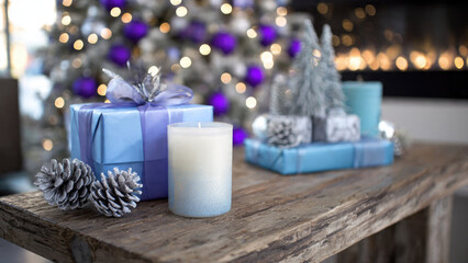 Elegant blue and purple holiday gifts, a candle, and silver decor accent a rustic wooden table against festive lights.