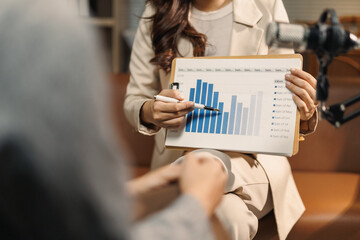 Business professional holding a clipboard, pointing to a bar chart during a meeting or podcast recording, analyzing financial data