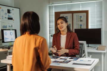 Two businesswomen collaborating in an office, discussing financial data and charts on papers, focusing on business growth strategy
