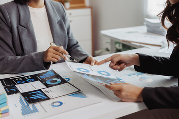 Two businesswomen discussing financial charts and graphs on documents. Collaborating on data analysis and strategic planning