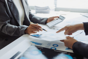 Business professionals collaborating, sharing insights, and analyzing financial graphs with a calculator on an office desk