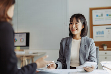 Asian businesswoman discussing financial data and business strategy with a colleague in a modern office environment