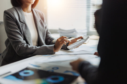 Businesswoman using a calculator and pen, analyzing financial data and charts with a colleague in a bright office environment