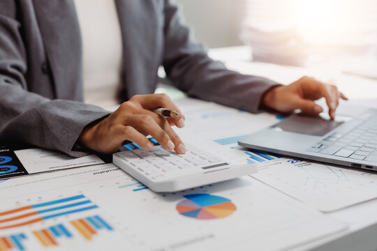 Business professional hands performing calculations on a desktop calculator while working with a laptop among financial charts and data reports - Powered by Adobe