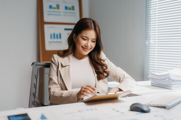 Asian businesswoman analyzing financial data and charts on documents at her office desk, embracing successful career development
