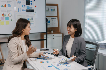 Two smiling businesswomen collaborating, discussing financial data with charts and graphs during a productive meeting in the office