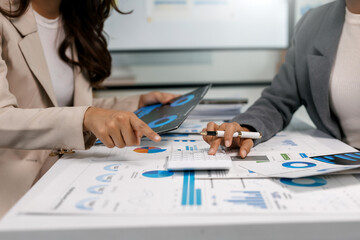 Business team collaborating, analyzing financial charts and data on papers and tablet while using a calculator in an office
