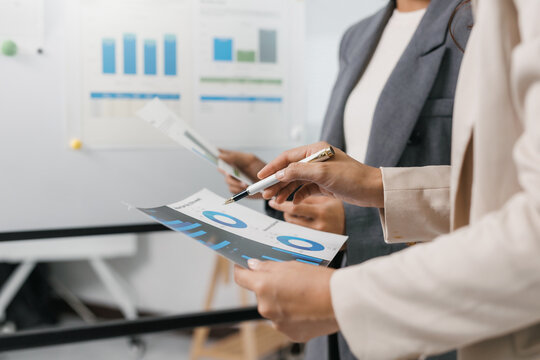 Professionals collaborating, reviewing financial reports and bar graphs in a corporate office, planning business strategy