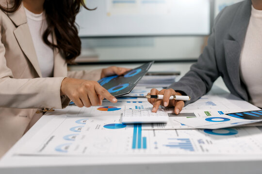 Business team collaborating, analyzing financial charts and data on papers and tablet while using a calculator in an office - Powered by Adobe