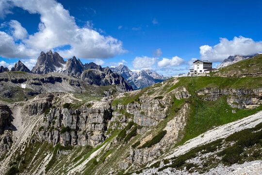 Scenic view of the Cadini di Misurina with Rifugio Auronzo hut on the ridge, seen from the Tre Cime circuit, Italy;  limestone cliffs, green slopes and against blue sky with clouds