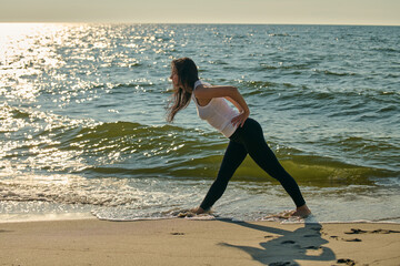Young woman practicing yoga stretch on Sandy Beach at Baltic Sea during sunset