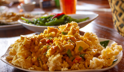 A serving of Ikan Asam Manis, a deep-fried Osphronemus goramy fish topped with sweet and sour sauce. The reddish glaze features chunks of Ananas comosus pineapple and onions on a white plate.