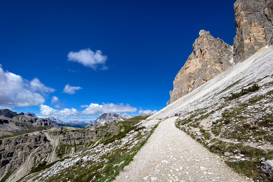 Scenic view of south-side hiking trail loop around Tre Cime di Lavaredo just past Rifugio Auronzo with Il Mulo peak; limestone walls and under a deep blue sky