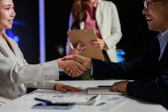 Professional colleagues making an agreement and closing a partnership deal during a late night negotiation in an office - Powered by Adobe