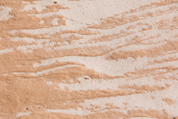 Wind blown white sand fills the cracks in pinkish brown rock, forming an abstract pattern in Southern Utah, USA.