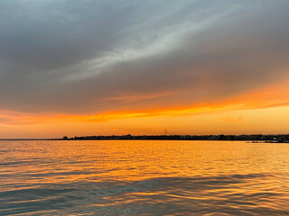 Serene sunset over calm waters, reflecting vibrant orange and yellow hues, creating a tranquil atmosphere at dusk with distant shoreline