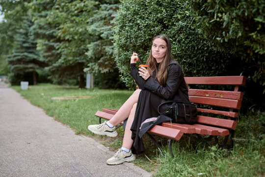 Young woman sitting on park bench drinking coffee cup during daytime