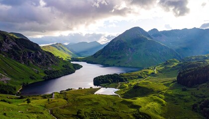 Aerial view of a stunning mountain landscape with a lake, green hills, and a dramatic sky. The scene is bathed in sunlight.