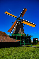 Traditional thatched windmill standing in a green field under a vibrant blue sky.