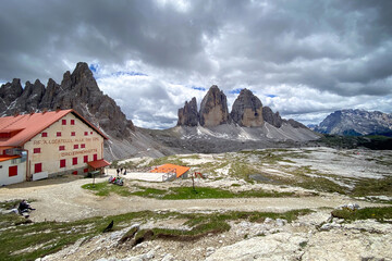 Scenic view of the Dreizinnenhütte (Rifugio A. Locatelli – S. Innerkofler), Italy with Monte Paterno beyond and Tre Cime di Lavaredo right; mountain hut from 1935 with red shutters against cloudy sky
