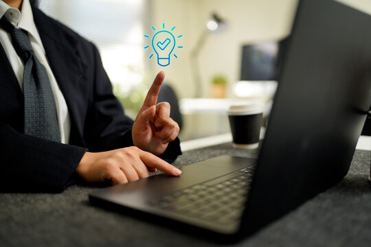 Businessman using laptop keyboard with hand gesture and glowing light bulb idea icon, creative innovation concept, digital technology work, online thinking and inspiration