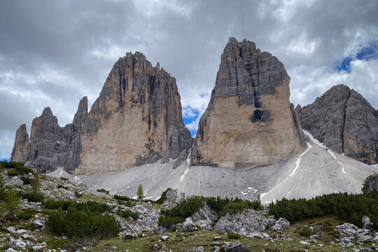 Close view of Tre Cime di Lavaredo in Italy, the three Dolomite towers rising above pale limestone scree and late snow against blue sky with clouds