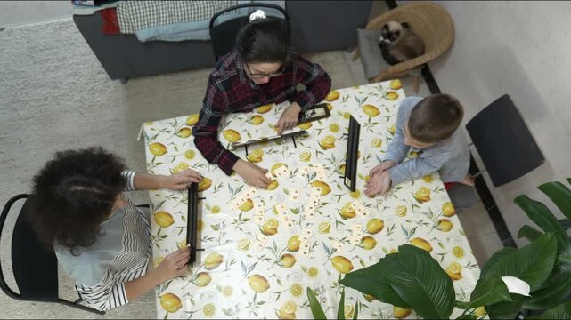 Family playing dominoes at dining table in Living Room during Daytime. Sister mother and brother enjoy an indoor board game