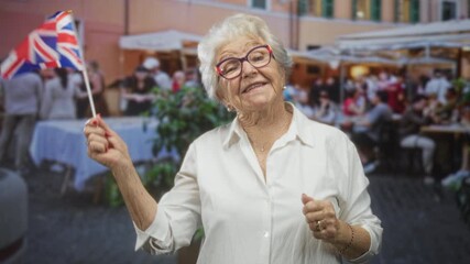 Elderly woman waves a small uk flag with bare hand at a busy street cafe, smiling and gesturing to onlookers; pride.