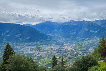 Scenic view over Merano (Meran) and the Burgraviato in the Adige Valley, Italy, with the Vinschgau (Val Venosta) and the Oetztal Alps beyond; towns, orchards and mountains under a cloudy sky