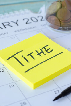 Tithe text on sticky note with coins and calendar. Christian finance, budget, and giving, biblical concept.