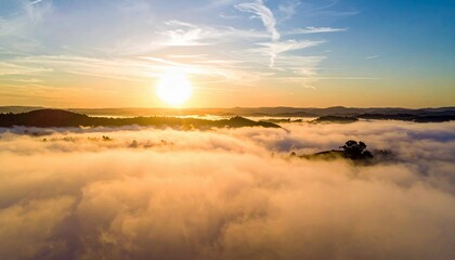 Aerial view of a beautiful sunrise over a landscape of mountains and clouds, with a warm golden glow.
