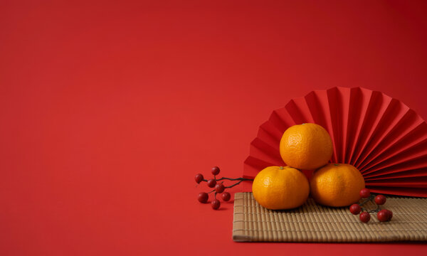 Three tangerines stacked with a red fan and berries festive arrangement for Chinese New Year isolated on a red background