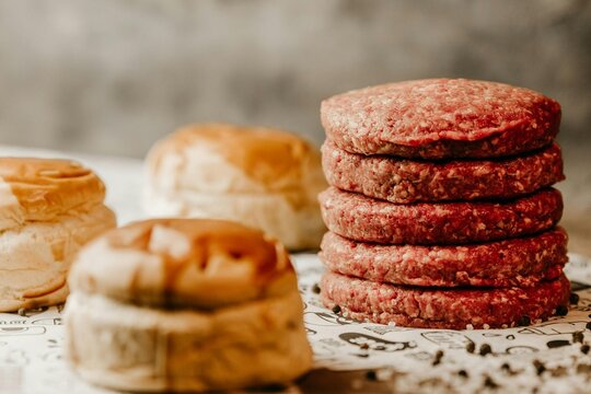Stack of raw hamburger patties with buns in the background ready for grilling and making burgers