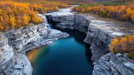 Aerial view of a waterfall cascading through a deep canyon, surrounded by colorful autumn trees. The scene captures the beauty of nature with a vibrant display