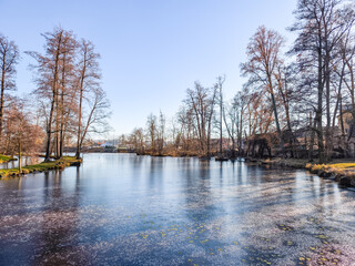 Blatna castle pond partially freezing, reflecting a clear blue sky and leafless trees on a winter day in czechia