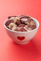 Heart-Shaped Bowl with Fresh Raw Chicken Hearts on Vibrant Red Background