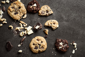 Homemade chocolate cookies, surrounded by cashew nuts, white and dark chocolate pieces, and cookie crumbs