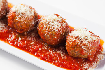 Close-up of meatballs with cheese and red sauce on a white plate, white background. 