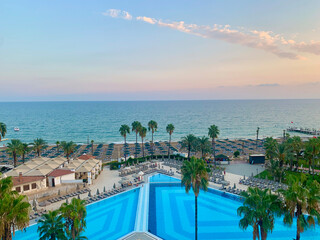 Sunset view of swimming pool with palm trees and sea horizon