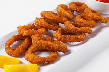 Fried onion rings with lemon wedges on a white plate, white background. 