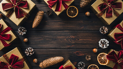 Fototapeta premium Christmas Frame with Gold Gifts Red Ribbons and Pine Cones on Dark Wooden Background.