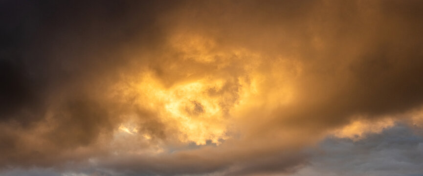 Epic panoramic view golden rain clouds during sunset or sunrise breaking through dark storm clouds creating powerful heavenly background with bright light