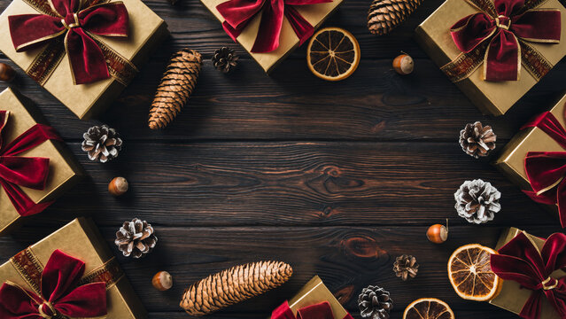 Christmas Frame with Gold Gifts Red Ribbons and Pine Cones on Dark Wooden Background.