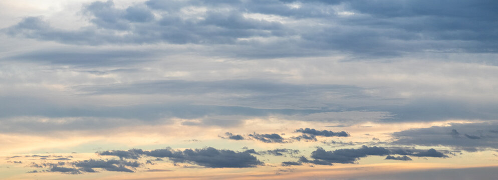 panoramic gray sky background with subtle pink-yellow hues on the horizon and multiple layers of clouds: from light transparent to dark and fluffy