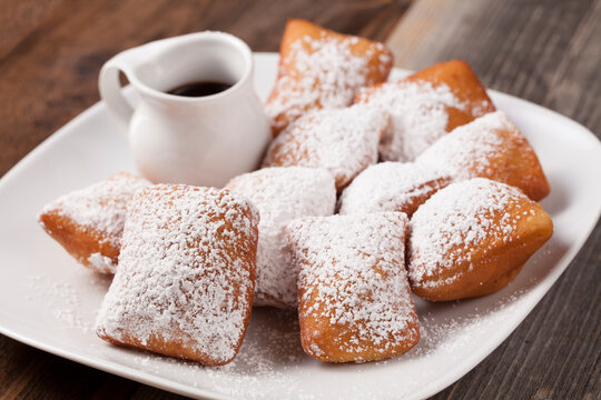  A white plate of French beignets With powder on a white plate against a wooden table background.